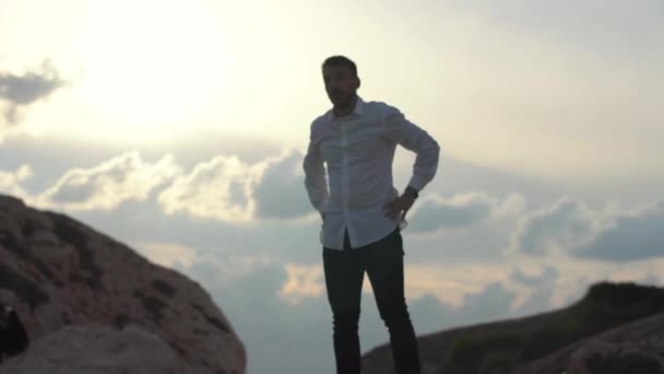 Beyaz gömlekli sakallı adam bulutların üzerinde bir dağın tepesinde duruyor. Genç şık adam dağın yüksek tepede durmak uzaklara bakmak. Kıbrıs. Baf — Stok video