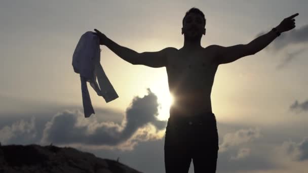 Camisa de hombre joven fuera grita libertad y aplaudiendo las manos en la alta colina de la montaña en la puesta del sol. El hombre tirando sus manos a un lado, disfrutando de la libertad, cree en el éxito futuro. Turista feliz en la cima de roca, victoria — Vídeos de Stock