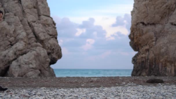 Knappe man kijkt rond tussen twee bergen aan de kust waar golven op rotsen kloppen. Cyprus. Paphos — Stockvideo