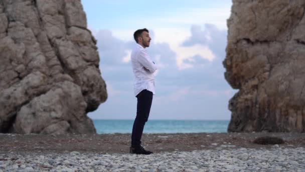 El joven mira a su alrededor entre dos montañas en la orilla del mar donde las olas golpean en las rocas. Chipre. Paphos. — Vídeos de Stock
