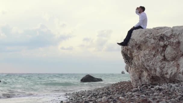 Gutaussehender, stylischer Mann, der auf den Felsen sitzt und eine fantastische Aussicht genießt, während er den Leuten mit dem Finger etwas zeigt. Zypern. Paphos — Stockvideo