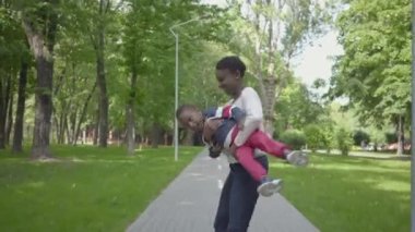 Afro-Amerikalı anne oğlunu kollarına döndürüyor. Anne ve çocuk hafta sonunu parkta dinlenerek geçiriyor..