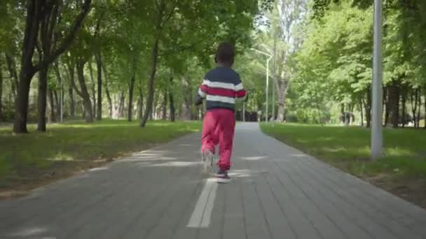 Visão traseira do menino afro-americano fofo fugindo, a câmera seguinte criança. Miúdo giro passar tempo ao ar livre sozinho. Lazer de verão — Vídeo de Stock