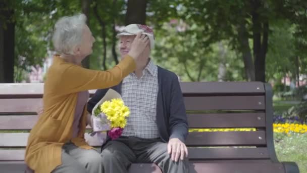 Old man kissing his woman with flowers on the banch in a spring park — Stock Video