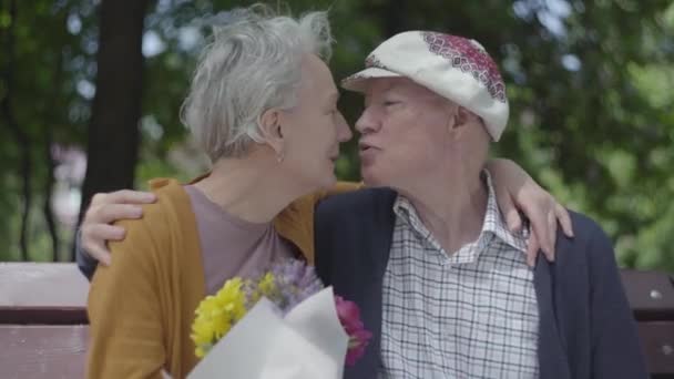 Ενήλικη γυναίκα κρατά ένα όμορφο μπουκέτο λουλουδιών, ενώ ο ηλικιωμένος σύζυγός της την αγκαλιάζει. Τρυφερή σχέση ενηλίκων ζευγάρι σε εξωτερικούς χώρους. — Αρχείο Βίντεο