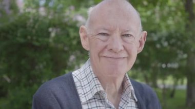 Parkta bir bankta oturan sevimli smilling yaşlı adam portresi. Sevimli olgun dedesi güneşli bir sıcak bahar günü açık havada istirahat.