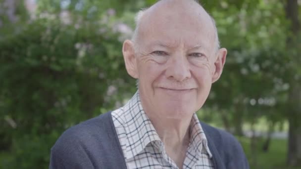 Retrato de un viejo lindo y oloroso sentado en un banco en el parque. Adorable abuelo maduro descansando en un soleado cálido día de primavera al aire libre . — Vídeo de stock