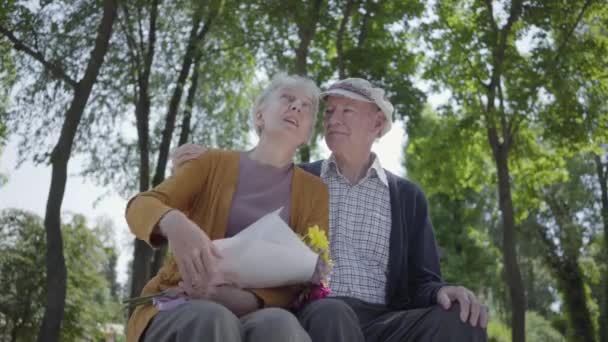Πορτρέτο ενός ώριμου ζευγαριού στην αγάπη καθισμένος σε ένα παγκάκι στο πάρκο. Αξιαγάπητη γυναίκα και γέρος μαζί. Τρυφερή σχέση ενηλίκων ζευγάρι σε εξωτερικούς χώρους. — Αρχείο Βίντεο