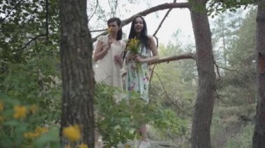 Portre kısa elbiseler içinde iki güzel kadın vahşi çiçekler ve doğanın tadını orman görünümlü kayalık zemin üzerinde duran. Sevimli kız birlikte açık havada yürüyüş hafta sonu harcama.