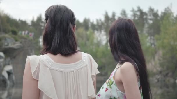 Dos adorables mujeres jóvenes usan vestidos de verano de pie en la parte superior de la roca y mirando la increíble vista de la naturaleza. Chicas guapas pasean fuera de la ciudad. Lindas novias pasando el fin de semana juntas al aire libre . — Vídeos de Stock