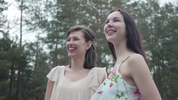 Retrato de dos mujeres jóvenes con olor lindo usan vestidos de verano de pie en la parte superior de la roca y mirando a la increíble vista de la naturaleza. Chicas guapas pasean fuera de la ciudad. Adorables novias al aire libre . — Vídeos de Stock