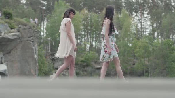 Retrato duas mulheres jovens encantadoras usam vestidos de verão em pé no topo do rock e olhando para uma vista incrível da natureza. Meninas bonitas caminham fora da cidade. Adoráveis namoradas passar fim de semana — Vídeo de Stock