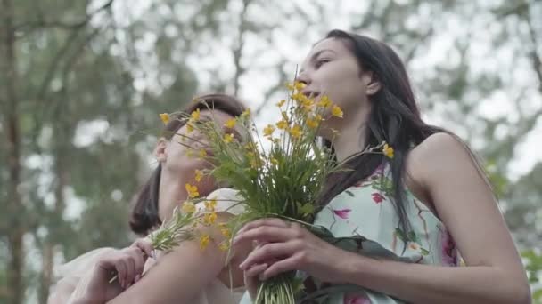 Ormanda muhteşem yabani çiçeklerle duran iki güzel kadın. Yavaş çekim. — Stok video