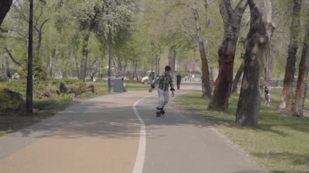 Adorabile ragazzo in abiti luminosi pattinaggio nel parco vicino al fiume. Tempo libero all'aperto. Il ragazzo si diverte da solo. Rallentatore — Video Stock