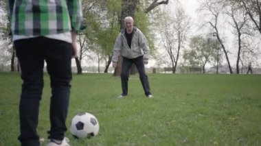 Küçük çocuk parkta babası ya da dedesi ile futbol ya da futbol oynuyor. Çocuk topu almaya çalışıyor ama adam ona izin vermiyor. Açık havada oynayan aile