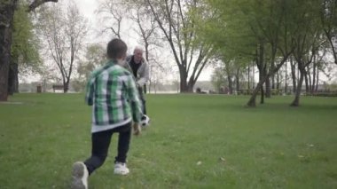 Torun topa vuruyor ve dedesi golü kaçırıyor. Mutlu sevimli çocuk futbol topu için yürürken ön planda atlama. Dışarıda eğlenen aile, aktif yaşam tarzı