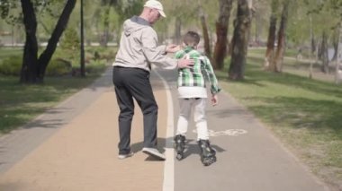 Büyükbabam torununa parkta paten kaymayı öğretiyor. Dışarıda boş zaman. Büyükbaba ve torunu birlikte vakit geçiriyorlar. Dışarıda boş zaman. Büyükbaba ve torunu birlikte vakit geçiriyor