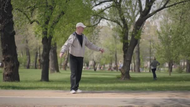 Kleiner Junge im karierten Hemd beim Inlineskaten im Park, sein Großvater fängt ihn ein und umarmt ihn. Aktive Freizeit im Freien. das Kind hat Spaß mit seinem Opa. alter Mann verbringt Zeit mit seinem Enkel — Stockvideo