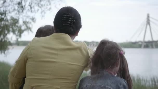 Avó adorável que sentado com duas netas bonitos no banco e olhando para o belo rio na floresta. Senhora abraçar seus filhos . — Vídeo de Stock