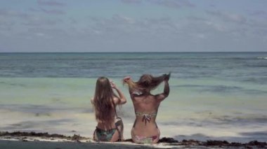 Seyşeller. Praslin Adası. Okyanusta oturan ve su yüzeyine bakan iki güzel kız. Tropikal ada lüks tatil.