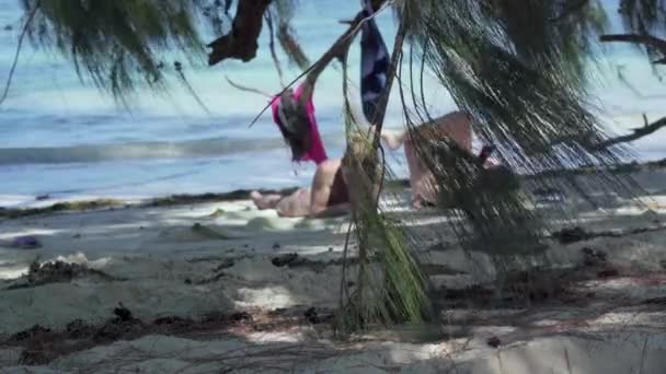 Сейшельские острова. Остров Праслин. Две девушки, лежащие в тени пальм, читают книги на берегу экзотического острова, расположенного в Индийском океане. . — стоковое видео