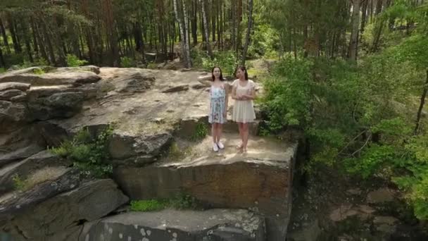 Bovenaanzicht van twee mooie vrouwen in korte jurken staande op rotsachtige grond. Schattige vriendinnen besteden het weekend samen wandelen buitenshuis. Schieten van de drone. — Stockvideo