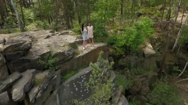 岩場に立つショートドレスを着た2人の美しい女性のトップビュー。愛らしいガールフレンドは、屋外を歩いて一緒に週末を過ごします。ドローンからの撮影. — ストック動画