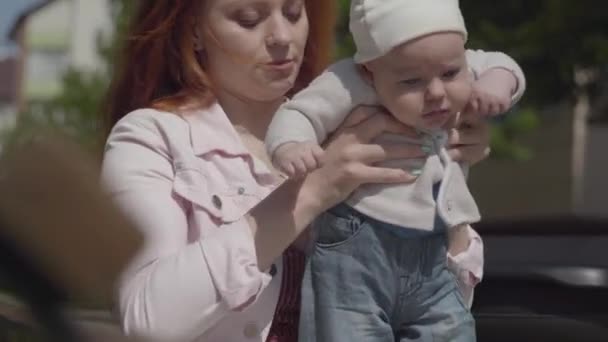 Portrait jolie jeune belle maman tenant adorable bébé dans ses bras et lui parlant par une journée ensoleillée de printemps à l'extérieur. Famille heureuse . — Video