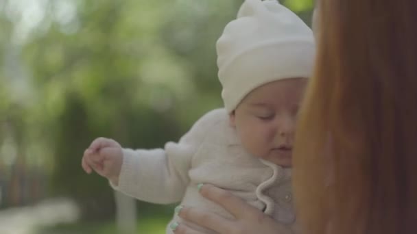 Redhead mamma Holding och kysser hennes söta bebis i famnen och prata med honom i en vårsolig dag utomhus. Lycklig familj. — Stockvideo