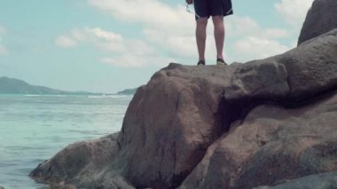 Seyşeller. Praslin Adası. Denizde kayanın üzerinde tanınamayan bir adam. Güzel deniz manzarası. Mavi temiz su. Turizm, tatil, seyahat konsepti