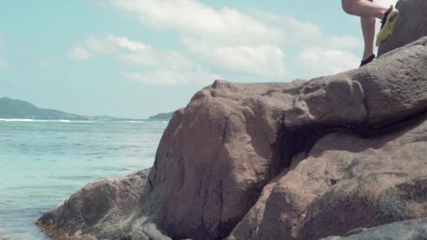 Seicheles. Ilha Praslin. Pernas de homem irreconhecível em pé sobre a rocha no mar. Bela paisagem marinha. Água limpa azul. Turismo, férias, viajar conceito — Vídeo de Stock