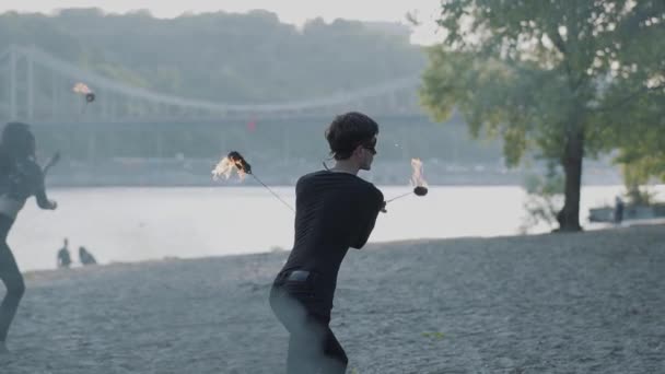 Unga Slim man i svart kläder och kvinna utföra en show med flamma stående på Riverbank. Skickliga fireshow konstnärer visar behärskning av jonglering och rörelse av eld på kvällen. Slow motion — Stockvideo