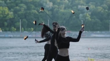 Ustaca adam ve siyah giysiler ve maskeler iki kadın nehir kıyısında ayakta iken alev ile bir gösteri gerçekleştirin. Usta fireshow sanatçılar hokkabazlık ve akşam yangın hareket ustaca gösteren