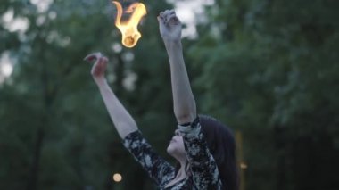 Sevimli genç Grace kız orman önünde alev ayakta bir gösteri performans. Ustaca itfaiyelernasıl sanatçı güçlü ateşli Jet exhaling. Yavaş hareket. Kadın ateş büyük akarsu dışarı nefes