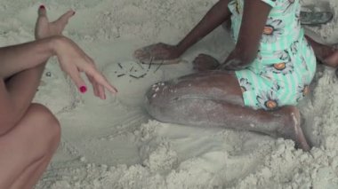 Seyşeller. Praslin Adası. Tanınmaz ince beyaz kadın sahilde kum Afrikalı Amerikalı kız ile oynuyor. Turist yerel ile iletişim kurar. Turizm, dinlenmek, tatil, seyahat