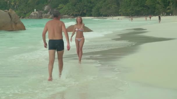 Seychellen. Praslin Island. Mooie gelukkige paar rustend op het strand op het eiland. Mooie vrouw in gestreepte badmode nemen de hand van haar man. De man en vrouw op het zandstrand. Toerisme, ontspannen — Stockvideo
