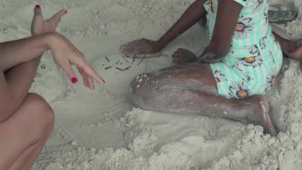 Seychelles. La isla Praslin. Mujer caucásica delgada irreconocible jugando con la chica afroamericana en la arena en la playa. El turista se comunica con el local. Turismo, relax, vacaciones, viajes — Vídeo de stock