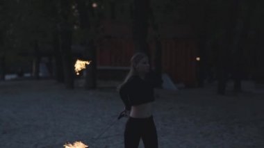 İnce vücut ile müthiş emin kız ağaçların önünde alev ayakta bir gösteri performans. Usta fireshow sanatçı hokkabazlık ve akşam yangın hareket ustaca gösteren. Yavaş hareket