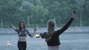 İki genç kadın nehir kıyısında duran alev topları ile bir gösteri yapıyor. Ustaca itfaiyelernasıl sanatçılar ateş hareket ustalığını gösteren. Yavaş hareket