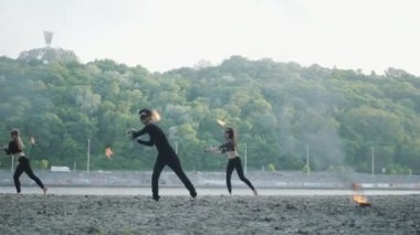 Genç ince adam ve iki güzel kadın aynı anda yol ve ormanın önünde ayakta iken alev ile göstermek gerçekleştirin. Usta fireshow sanatçılar akşam yangın hareket ustaca gösteren