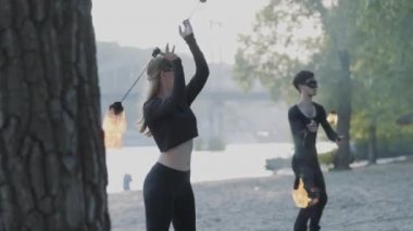 Siyah giysiler genç güzel kız ve yakışıklı adam nehir kıyısında alev ayakta gösterisi performans. Adam başını üzerinde güçlü ateşli Jet exhaling iken ateş topu Golding kadın. Yavaş hareket