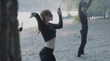 Siyah giysiler genç güzel kız ve yakışıklı adam nehir kıyısında alev ayakta gösterisi performans. Adam başını üzerinde güçlü ateşli Jet exhaling iken ateş topu Golding kadın. Yavaş hareket