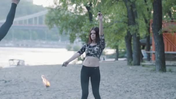 Portret van jonge schattige vrouw in het masker het uitvoeren van een show met vlam in de voorkant van bomen. Bekwame fireshow kunstenaar die danst met brand ventilators in openlucht toont. Slow Motion — Stockvideo