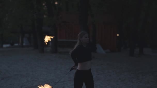 Удивительная уверенная девушка с худым телом выполняет шоу с пламенем, стоящим перед деревьями. Умелый артист фейерверка демонстрирует мастерство жонглирования и движения огня вечером. Медленное движение — стоковое видео