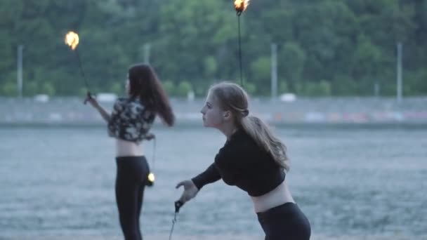 강둑에 서서 불꽃공을 들고 공연을 하는 두 명의 청녀. 화재의 움직임의 숙달을 보여주는 숙련 된 불꽃 예술가. 슬로우 모션 — 비디오