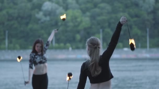 Två unga kvinnor som utför en show med flammor bollar som står på Riverbank. Skickliga fireshow konstnärer som visar behärskning av rörelse av eld. Slow motion — Stockvideo