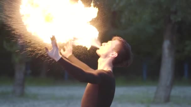 Junger Mann in schwarzer Kleidung, der eine Show mit Flamme am Flussufer aufführt. Geschickter Feuershow-Künstler, der am Abend einen mächtigen Feuerstrahl ausstößt. Zeitlupe. Männchen atmet großen Feuerstrom aus — Stockvideo