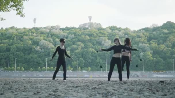 Jovem homem magro e duas mulheres bonitas realizam simultaneamente show com chama enquanto estão em frente à estrada e bosques. Artistas de fogos de artifício habilidosos mostrando domínio do movimento de fogo à noite — Vídeo de Stock