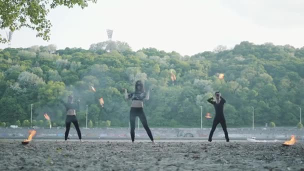 Jeune homme mince et deux belles femmes exécutent simultanément spectacle avec flamme tout en se tenant devant la route et les bois. Artistes de feu habiles montrant la maîtrise du mouvement du feu dans la soirée — Video