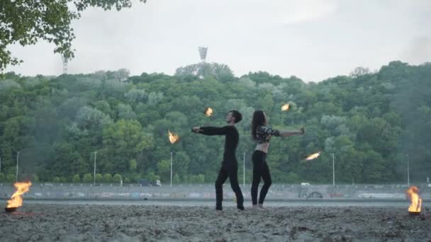 Homem magro jovem em roupas pretas e mulher atraente executar show com chama ao ar livre. Artistas de fogos de artifício habilidosos mostrando domínio do movimento de fogo de costas para trás. Câmara a aproximar-se — Vídeo de Stock